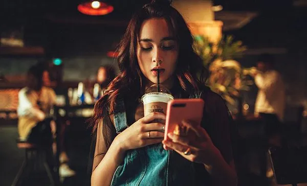 девушка пьет коктейль с телефоном в руках